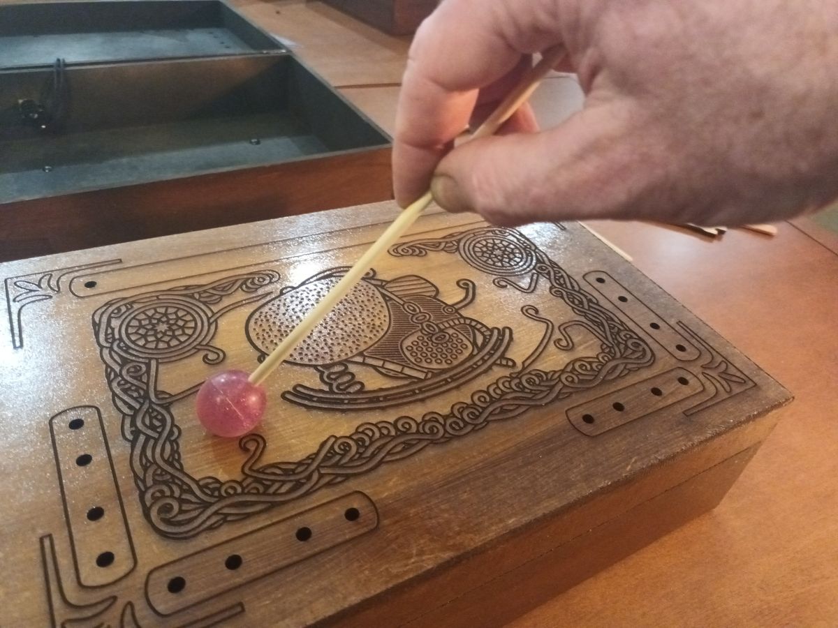 Mão segurando a baqueta de fricção com uma bola pula-pula rosa sobre o tampo gravado.